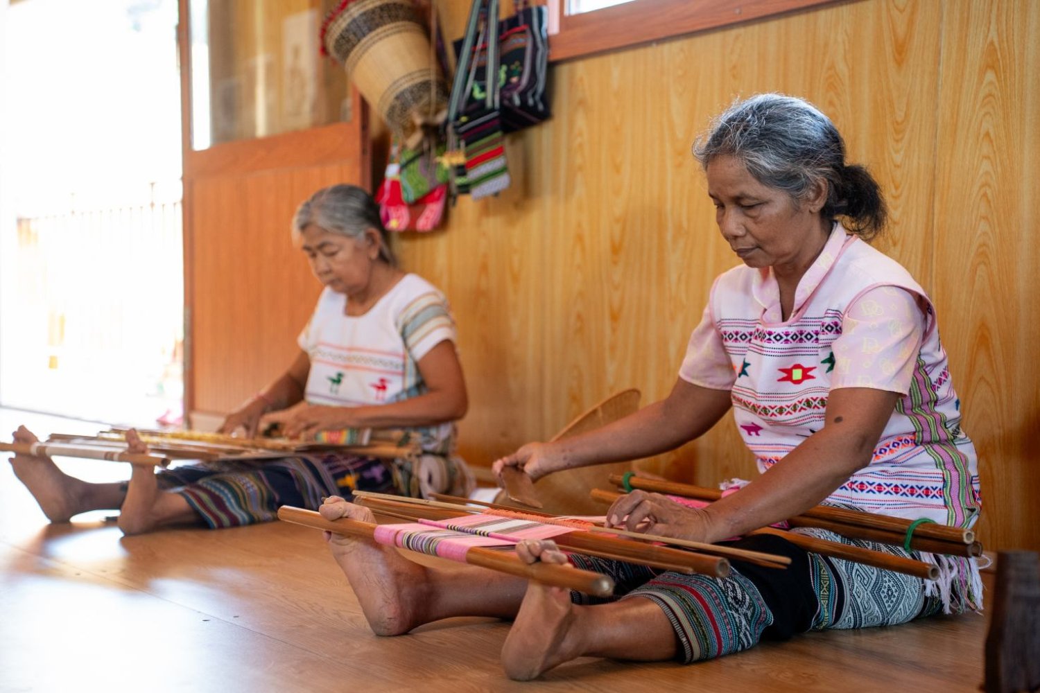 Ma brocade artisans sit on the floor as they weave textiles by hand using traditional techniques.